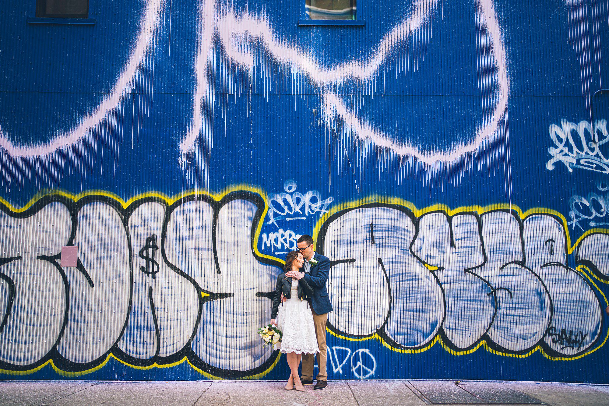 Stunning bride in leather jacket in front of a NYC graffiti wall by Sascha Reinking Photography, New York Elopement Photographer