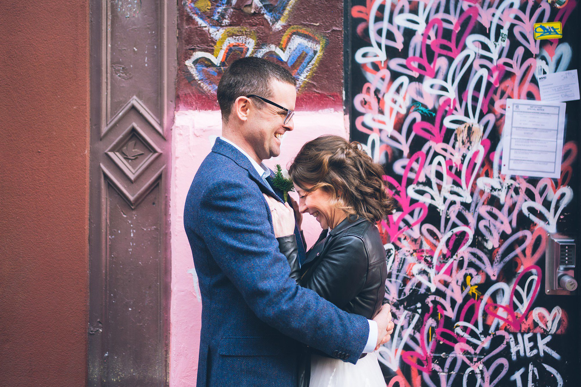 Happy wedding couple in front of a heart graffiti wall in New York City by Sascha Reinking Photography, New York Elopement Photographer